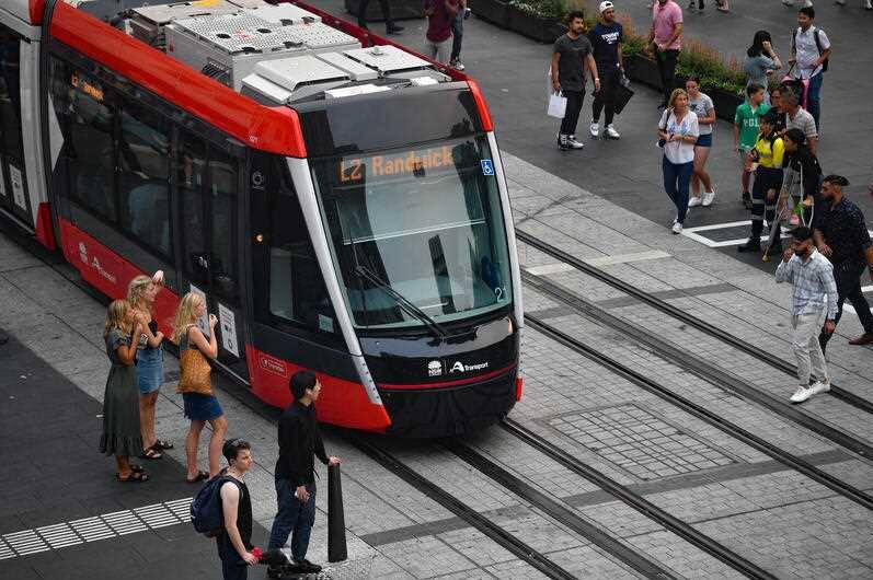 A tram moving through George Street surrounded by pedestrians.