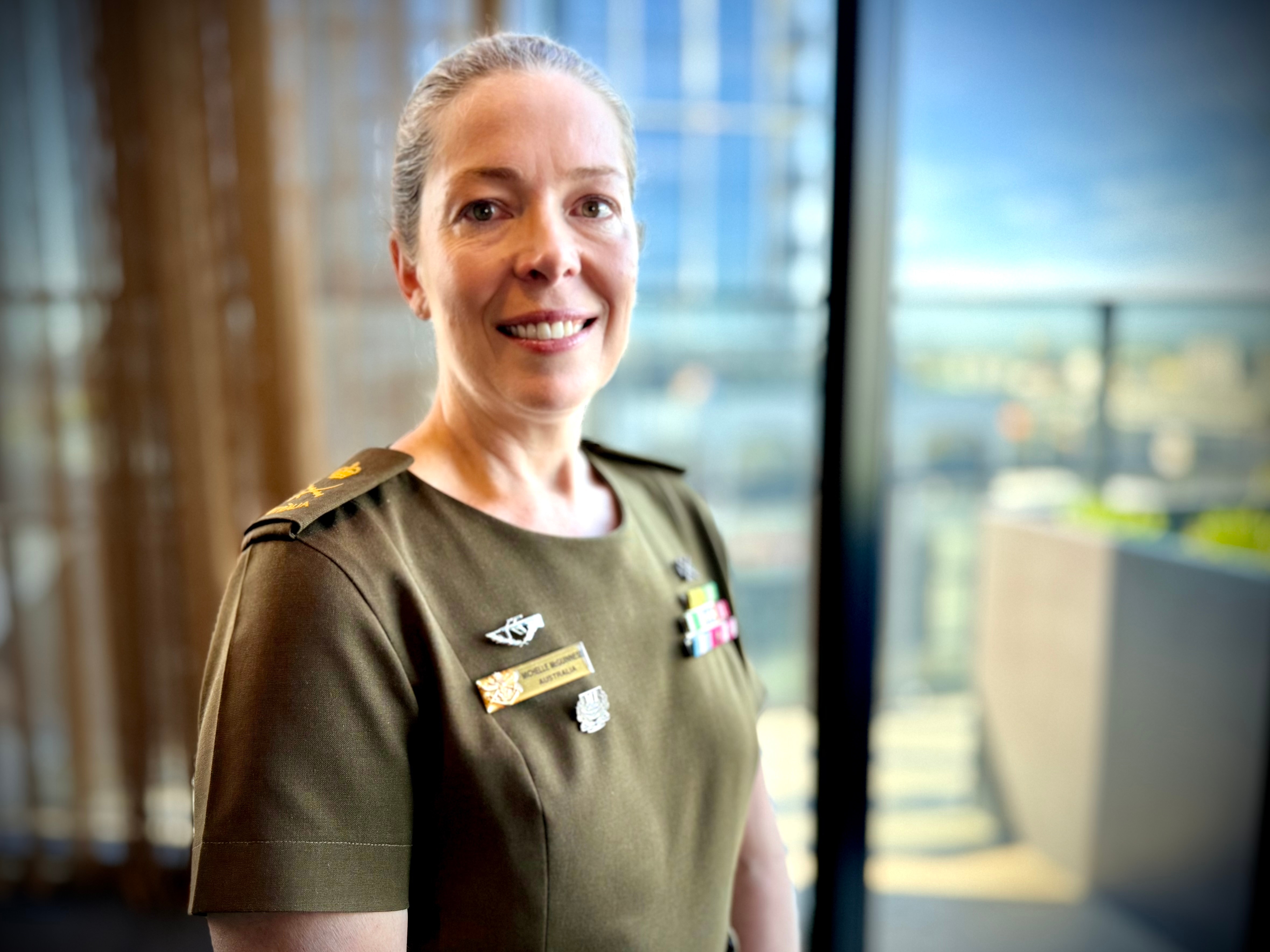 Smiling Michelle in khaki uniform, hair slicked back, has medals and rank pinned on both sides.