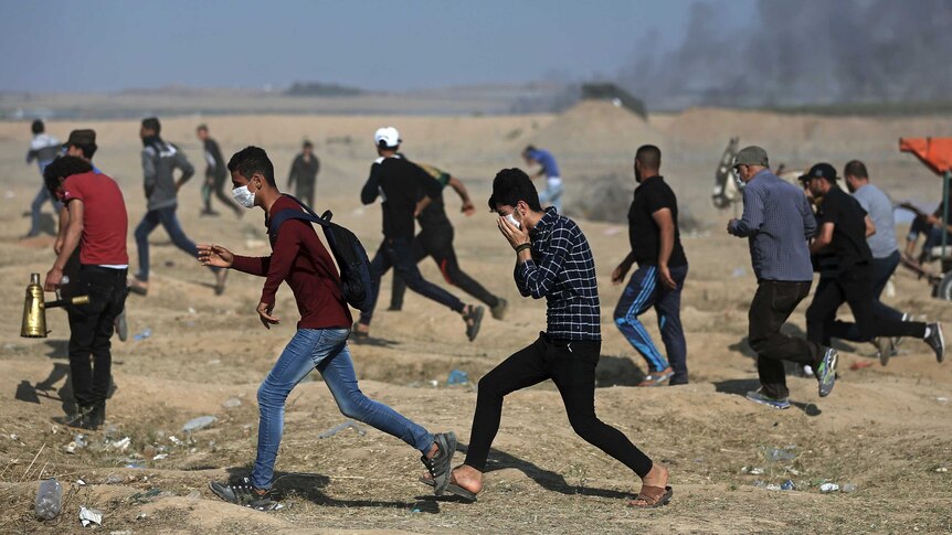 Palestinian protesters run for cover from teargas.