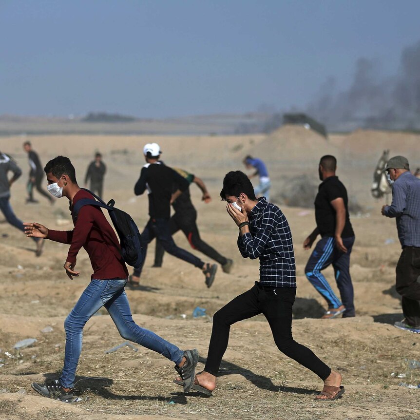 Palestinian protesters run for cover from teargas.