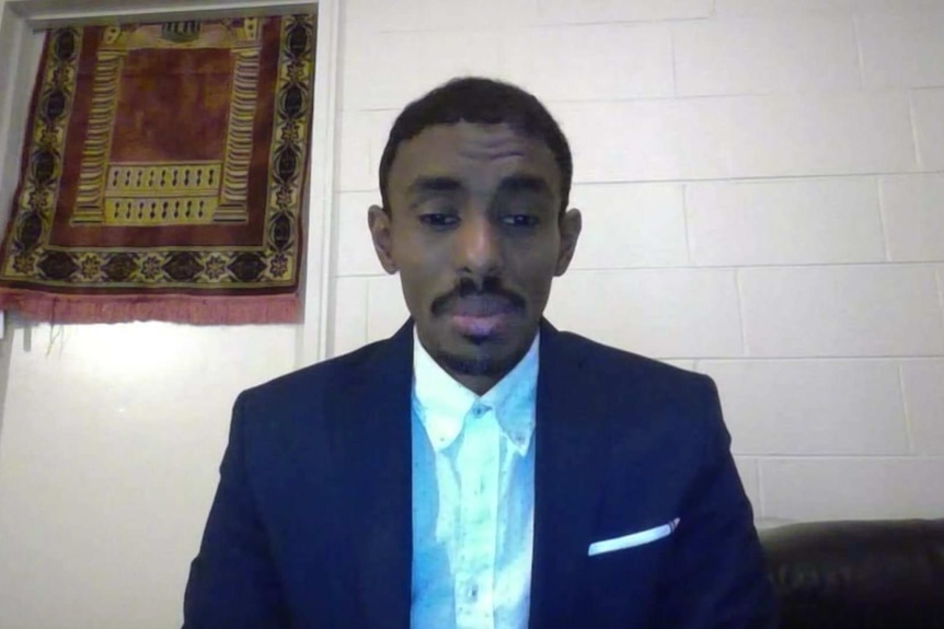 Ahmed Dini wearing a blue suit jacket and business shirt in a video call.