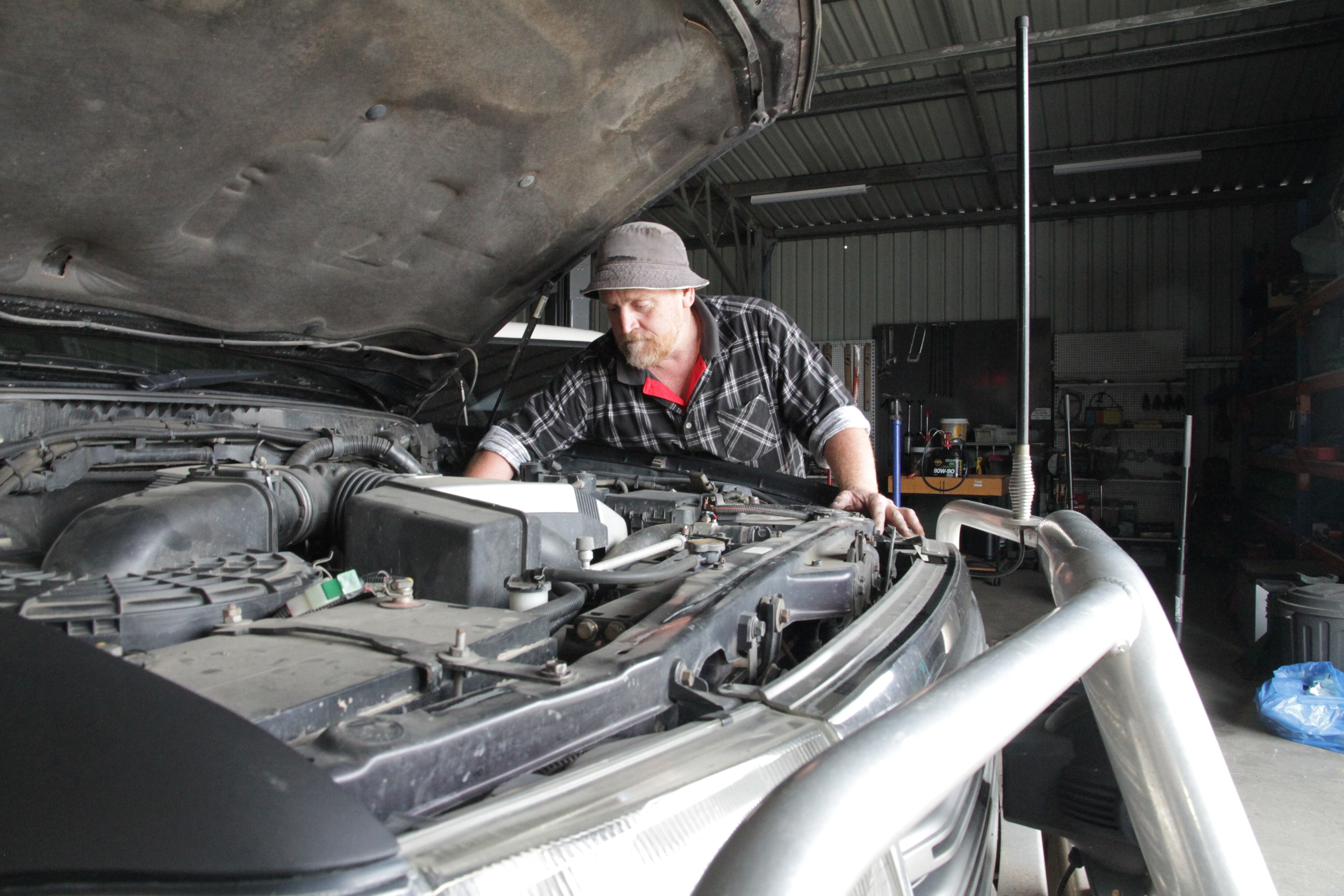 A man leans over the open bonnet of a car and looks inside