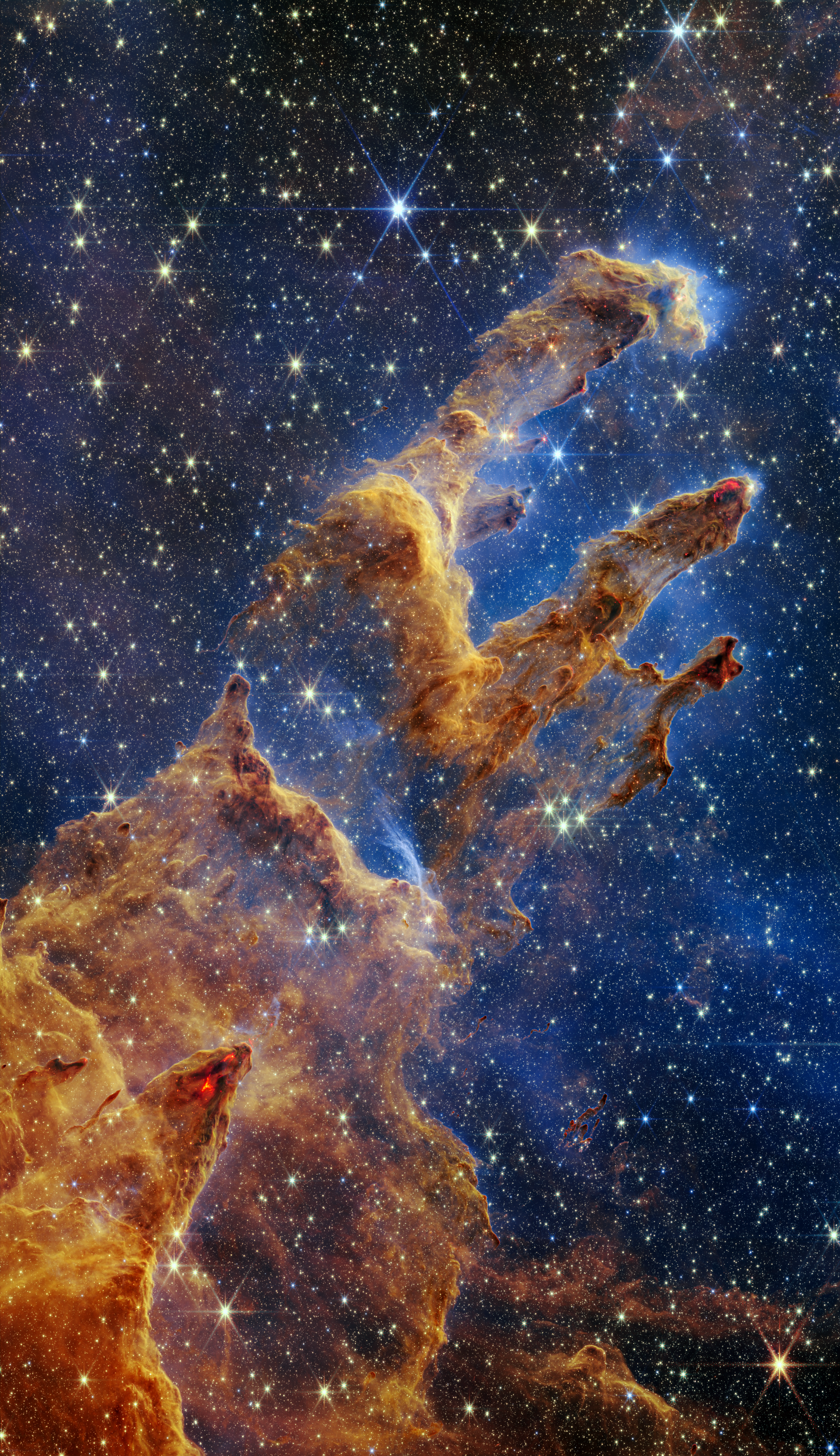 An image of the Pillars of Creation, with orangey-brown dust clouds on a dark blue, starry background. 