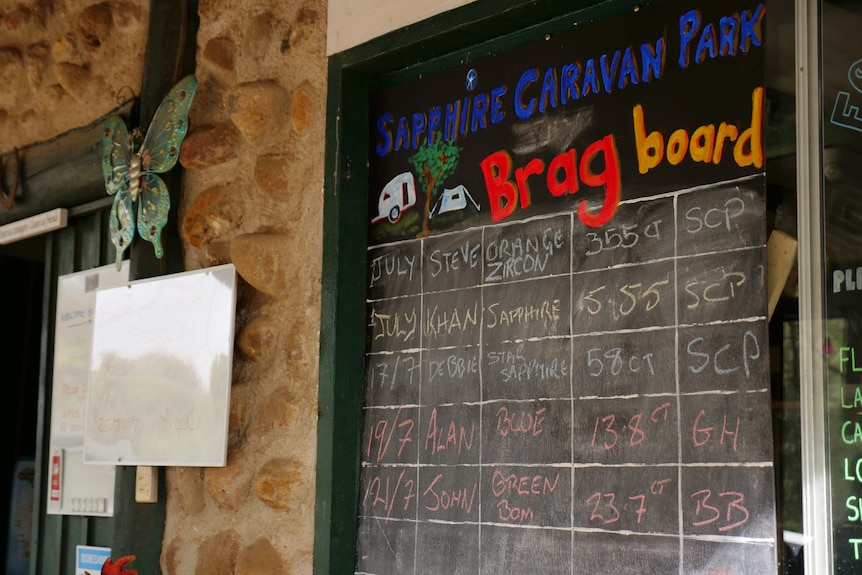 A chalk board that says Sapphire Caravan Park Brag Board with month, names, type of stone and carot.