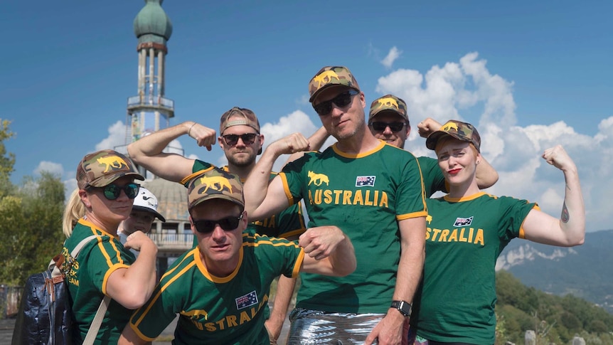 Six adults wearing green and gold sporting uniforms pose with their muscles flexed.