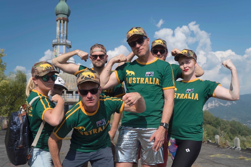 Six adults wearing green and gold sporting uniforms pose with their muscles flexed.