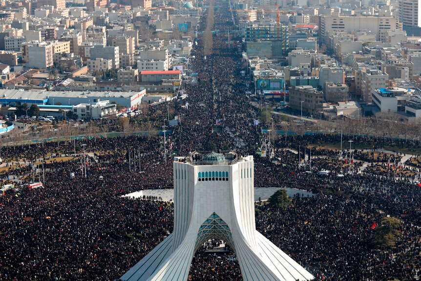 An aerial photo shows the curvilinear Azadi Tower surrounded by tens of thousands of people in a surrounding circular park.
