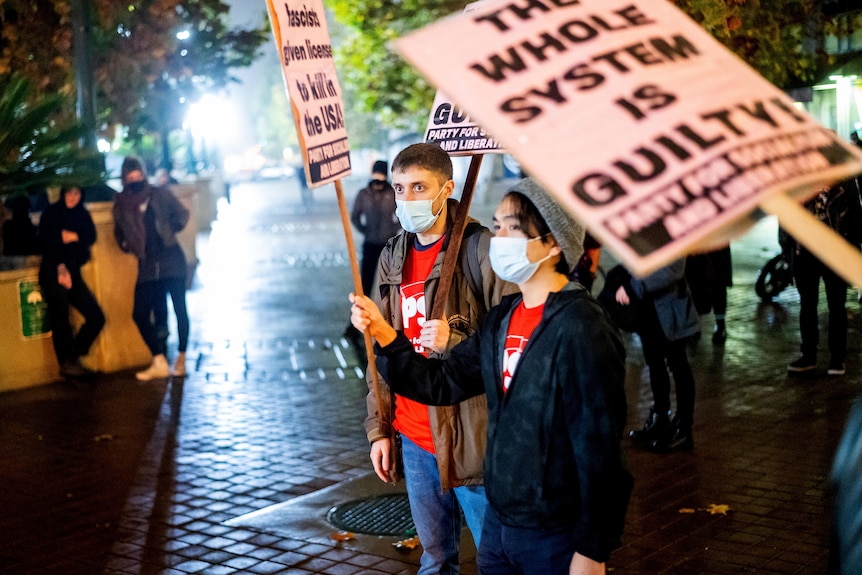 People hold placards including one that reads 'the whole system is guilty'