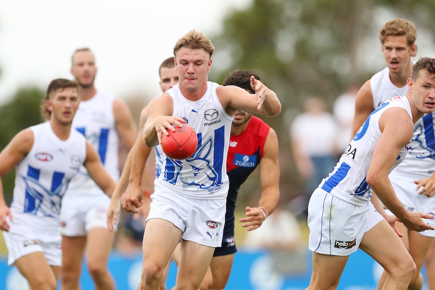 A young AFL player looks down at the ball as he runs and gets ready to drop it for a kick.