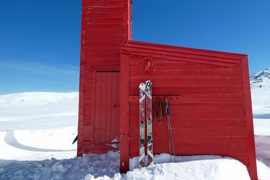 A red hut sits in a field of snow.