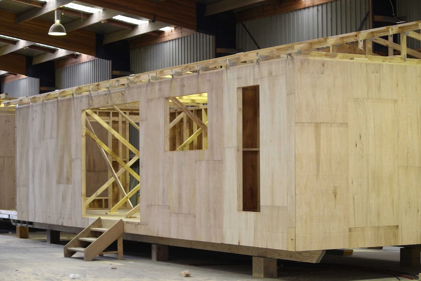 The wooden frame of an affordable accommodation unit under construction inside a shed.