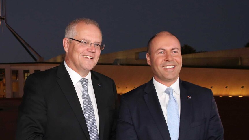 Wearing suits and smiling, Scott Morrison and Josh Frydenberg stand outside Parliament House before dawn.