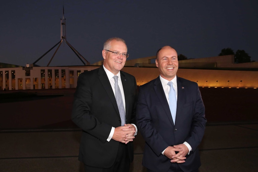 Wearing suits and smiling, Scott Morrison and Josh Frydenberg stand outside Parliament House before dawn.