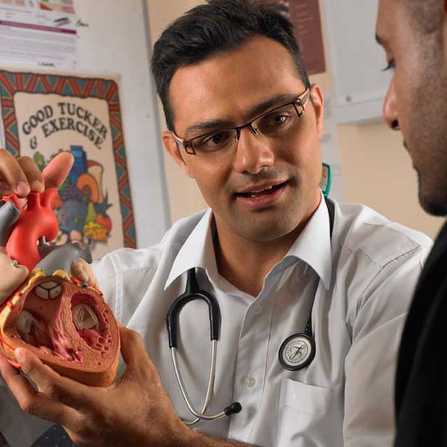 A male, Aboriginal doctor showing a heart model to another male.