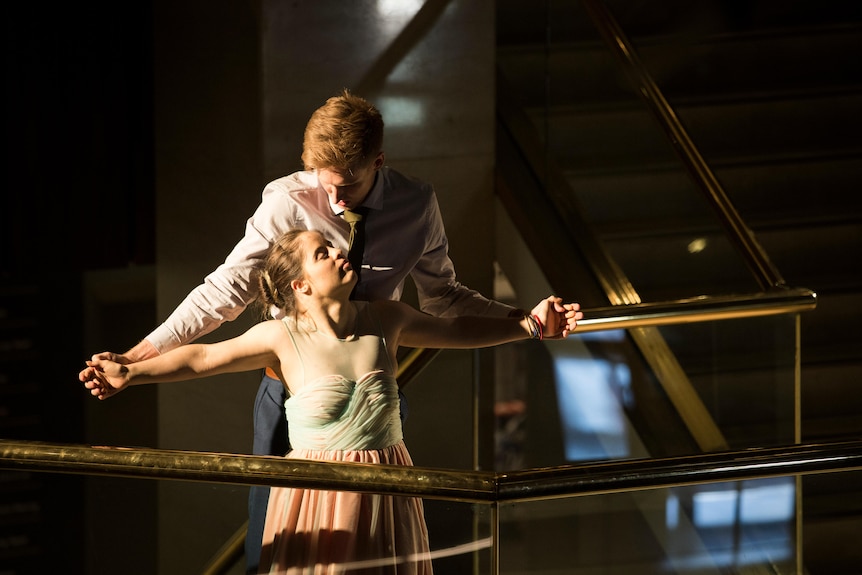 A white man with red hair, wearing a white shirt, dances with a white woman with brown hair, in a pastel dress.