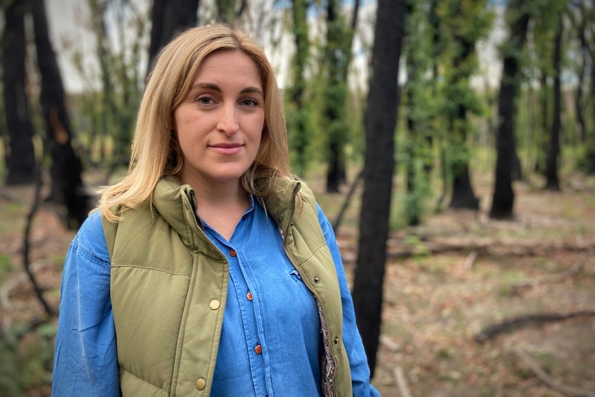 Casey Kirchoof stands among blackened trees that are spouting green shoots.