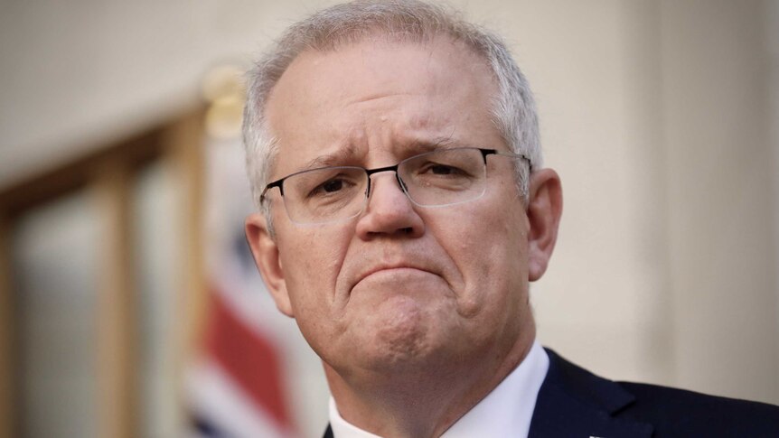 Scott Morrison, wearing a blue tie, frowns while standing in the PM's courtyard