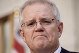 Scott Morrison, wearing a blue tie, frowns while standing in the PM's courtyard