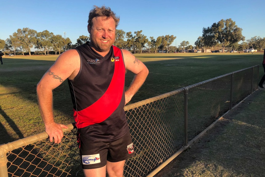 Man standing against fence in black and red football jumper at sunset