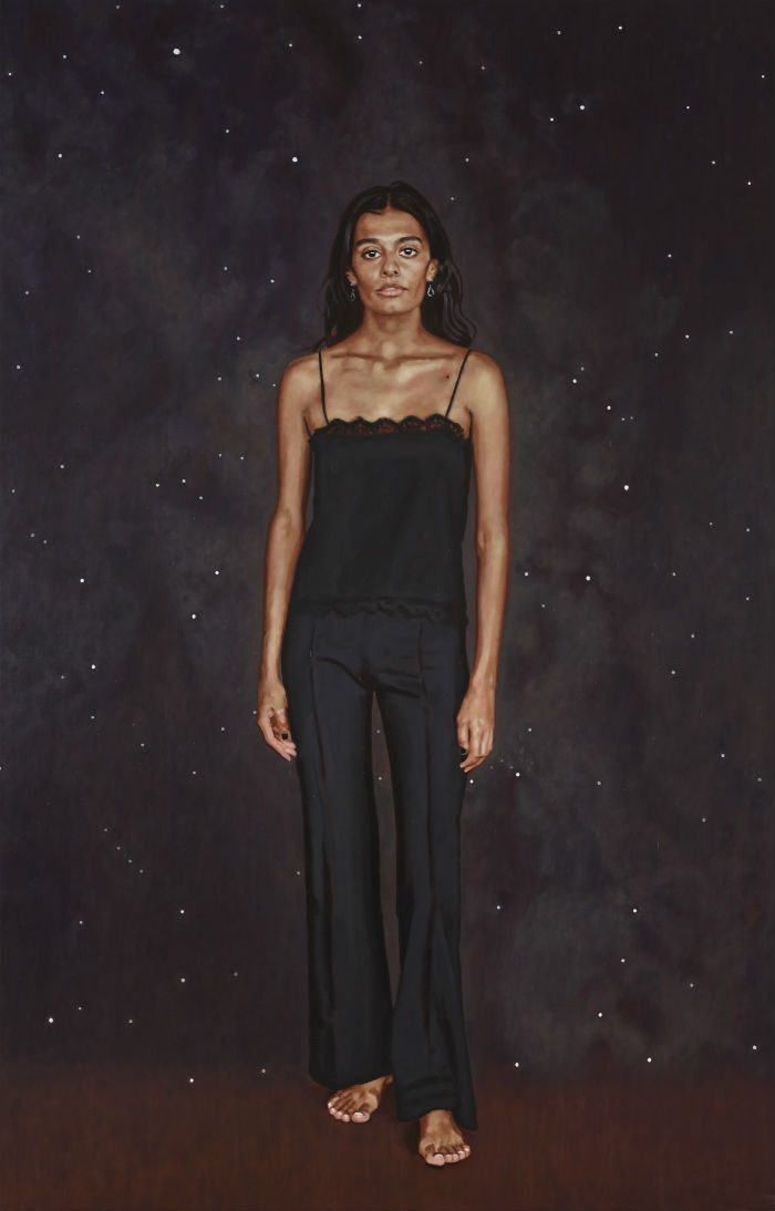 Madden stands in a black camisole and black pants against a starry background.