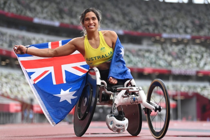 Woman draped in Australian flag poses in racing wheelchair on running track