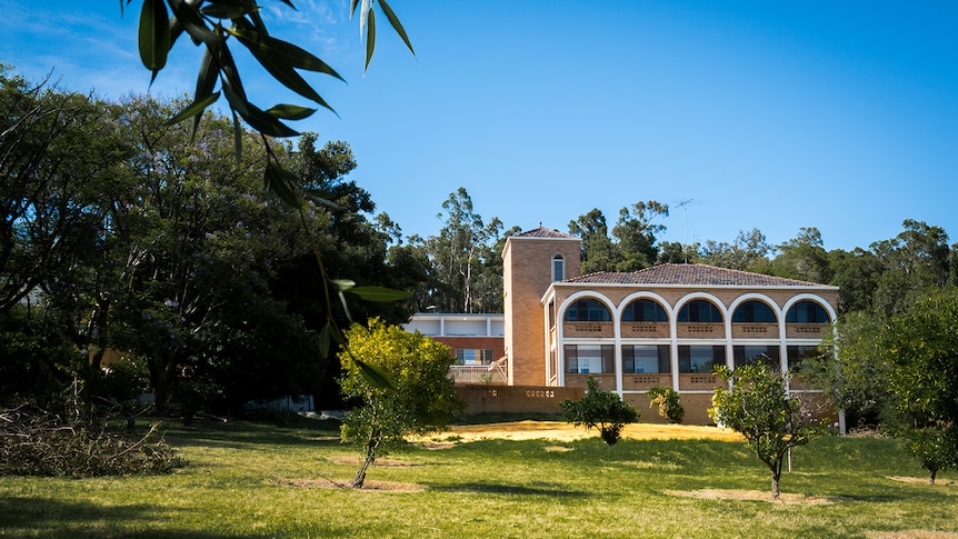 A big, old-fashioned building with arches – a former convent – in a grassy field surrounded by trees.
