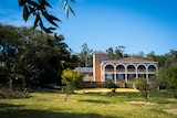 A big, old-fashioned building with arches – a former convent – in a grassy field surrounded by trees.