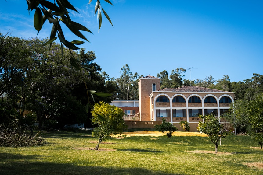A big, old-fashioned building with arches in a grassy field surrounded by trees.