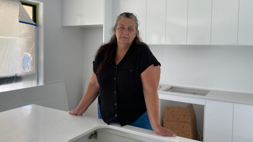 A woman stands in an unfinished modern white kitchen.