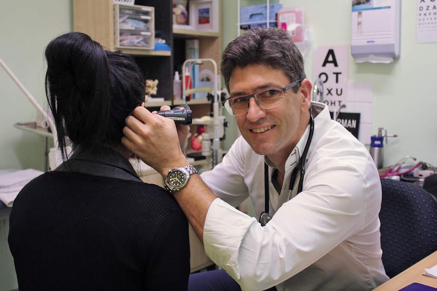 A doctor looks into the ear of a patient who has her back to us