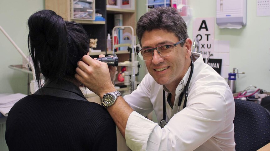 A doctor looks into the ear of a patient who has her back to us