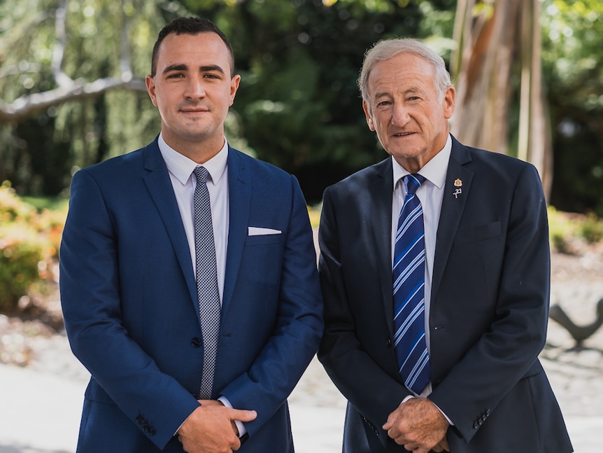 Two men in blue suits stand next to each other