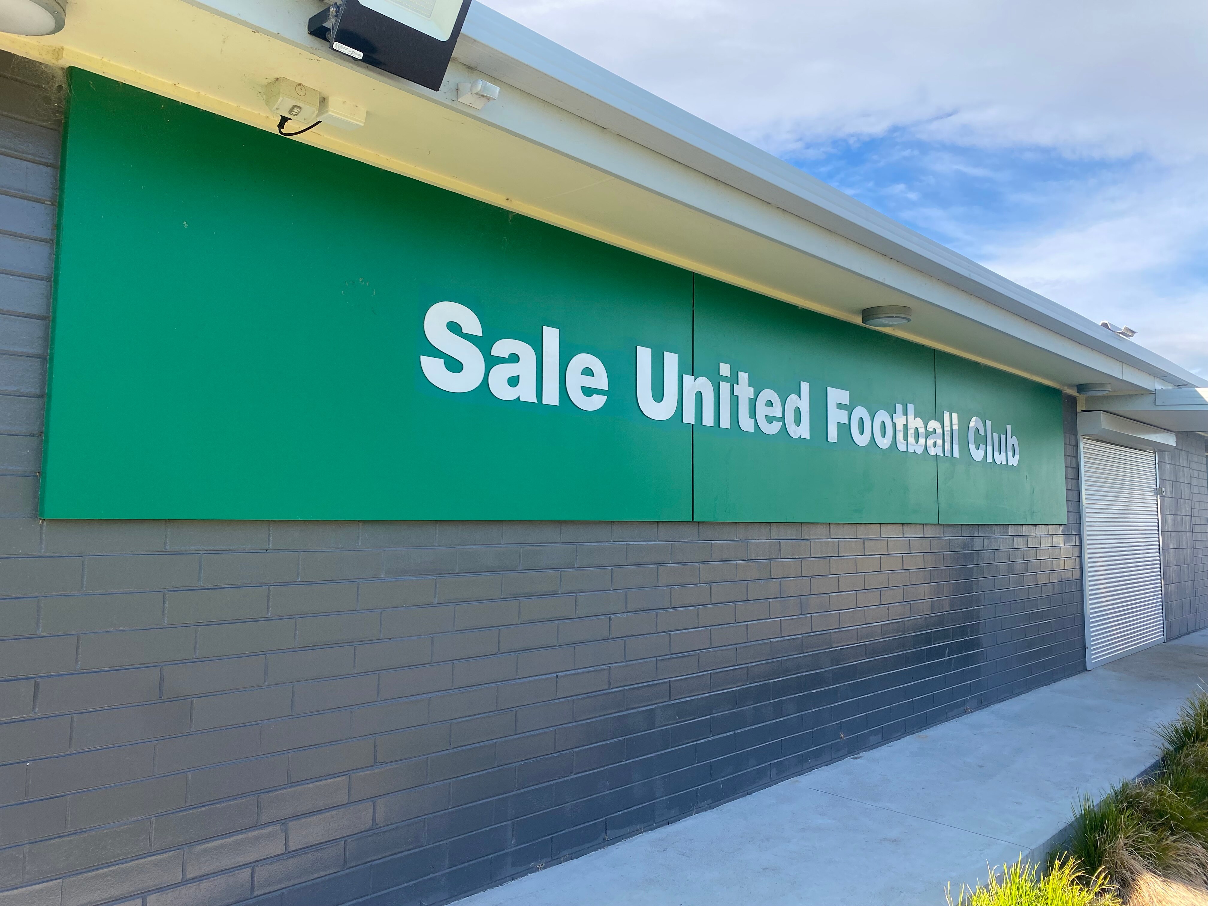 A gray club hall building with a large green sign reading Sale United Football Club