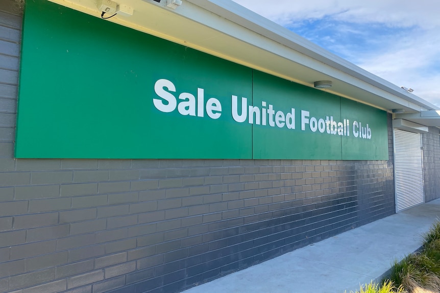 A grey clubroom building with a large, green sign that says Sale United Football Club