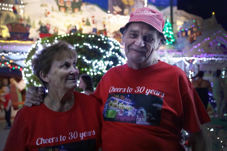 An older man and woman smile in front of a well lit house