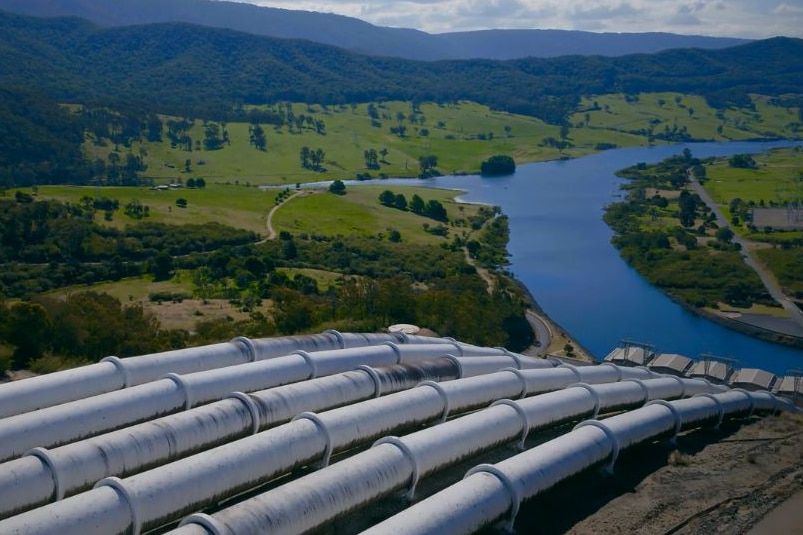 Six large pipes running down a hill toward a river.