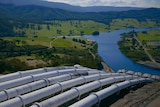 Six large pipes running down a hill toward a river.