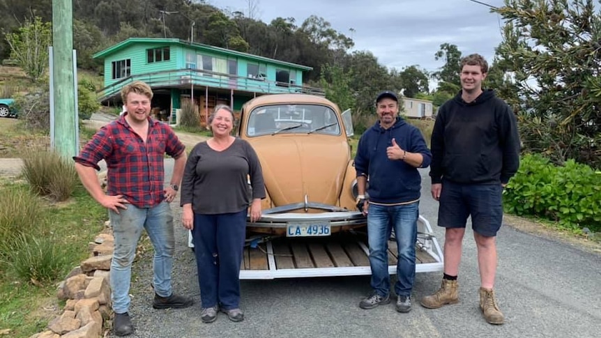 Four people stand with the VW bug on a trailer ready to head up to Launceston