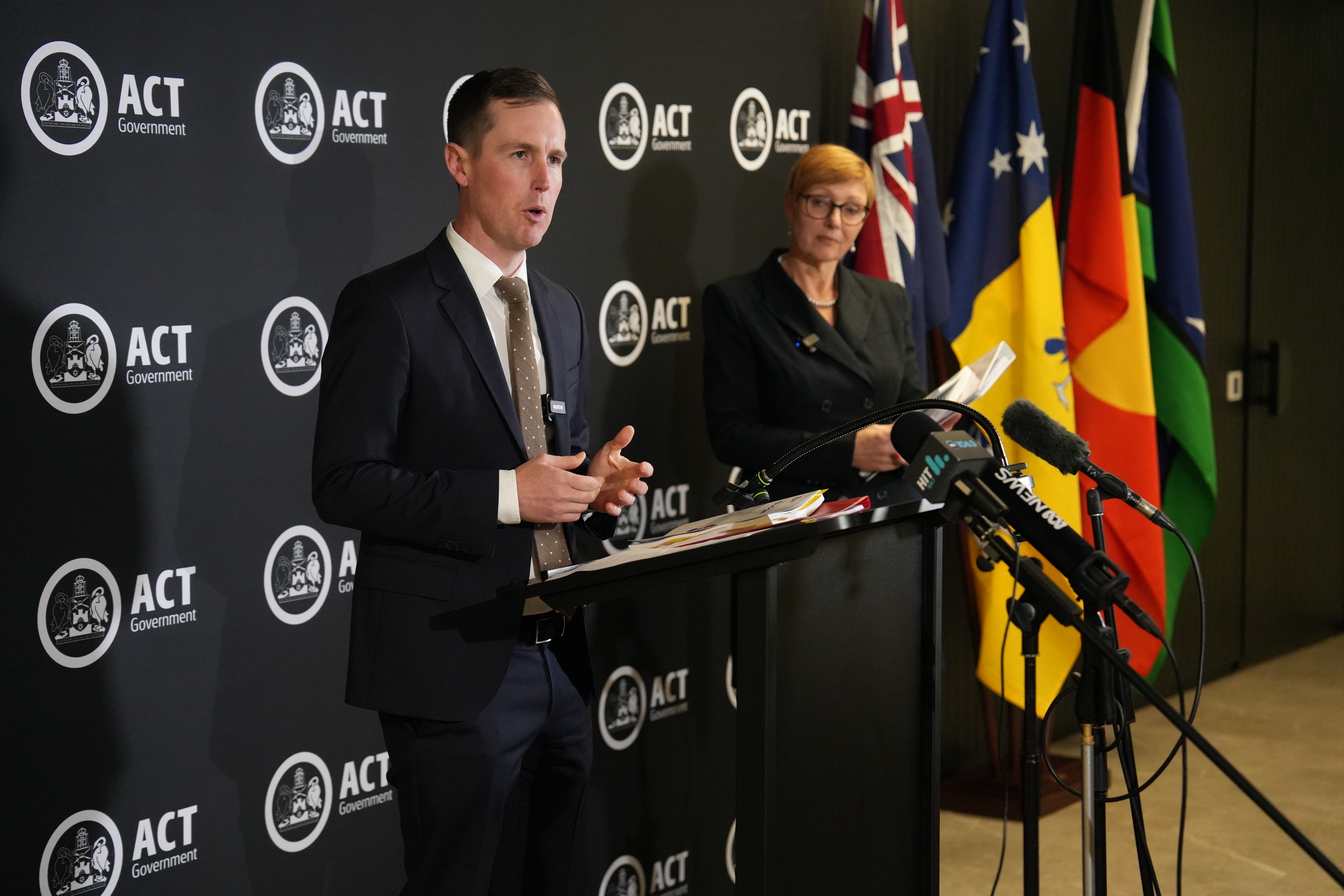 A man and a woman in business attire stand near a microphone.