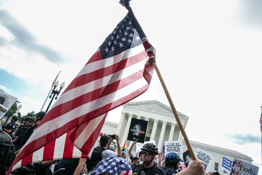 A US flag is carried past a big crowd outside the US Supreme Court