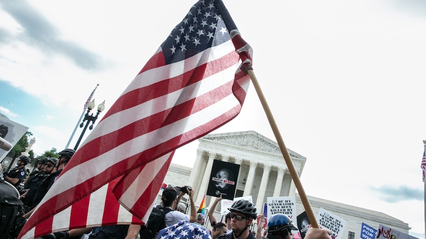 A US flag is carried past a big crowd outside the US Supreme Court