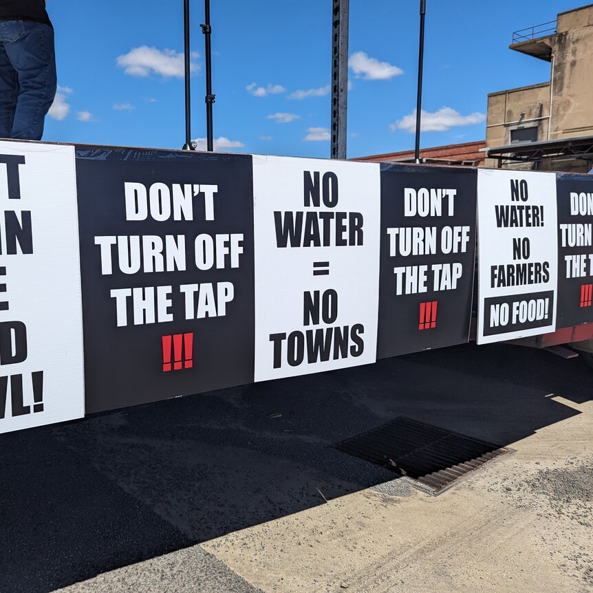 Signs that say "Don't drain the food bowl", and "Don't turn off the tap" on a stage at a protest against water buybacks