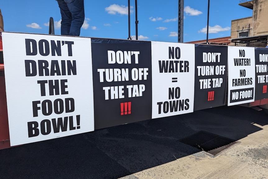 Signs that say "Don't drain the food bowl", and "Don't turn off the tap" on a stage at a protest against water buybacks