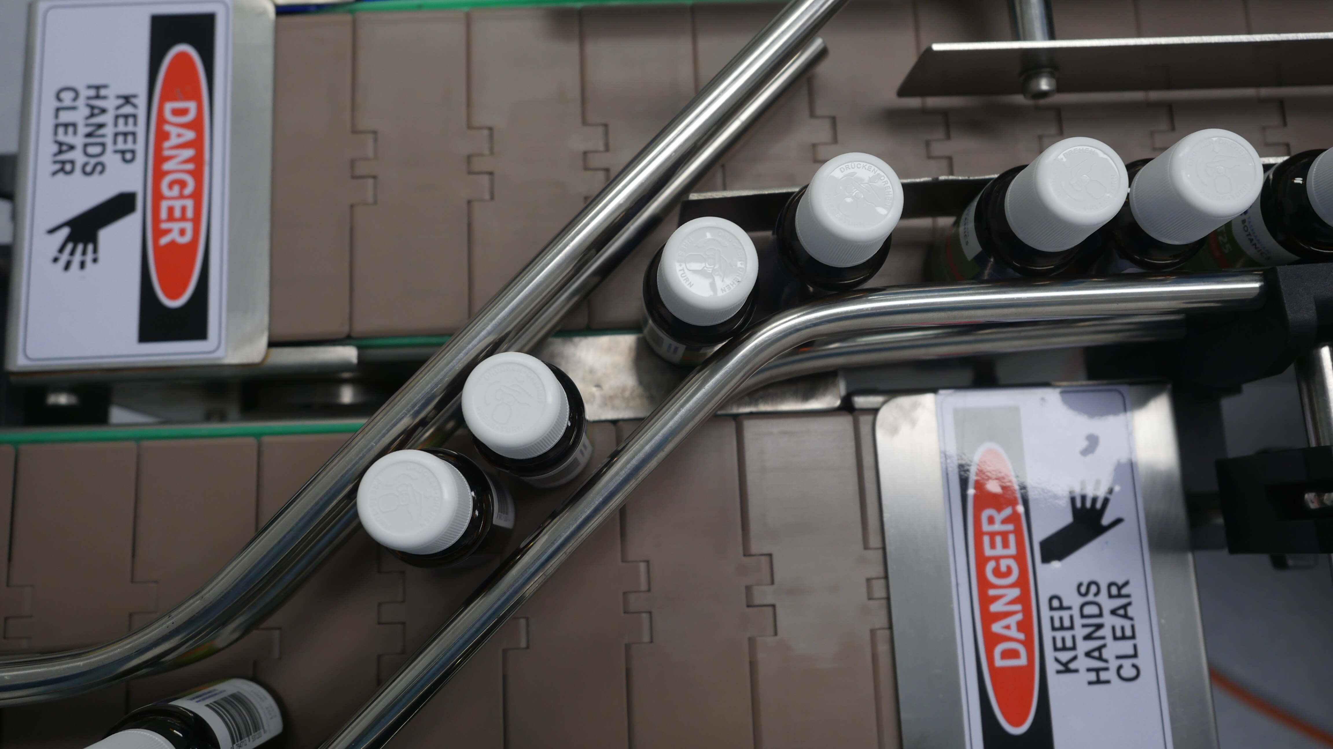 birds eye view of a conveyor belt transporting small dark glass bottles with white plastic caps 