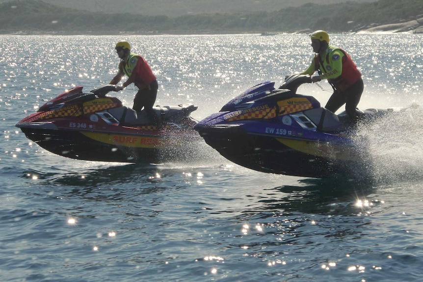 Two Albany Surf Life Saving Club members ride jet skis on the ocean wearing hi-viz gear and helmets.