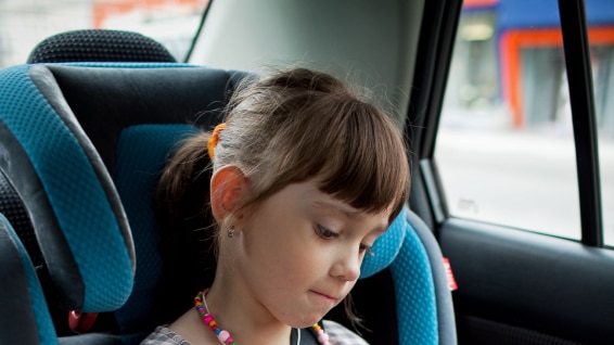 A young girl sitting in the back seat of a car in a car seat.