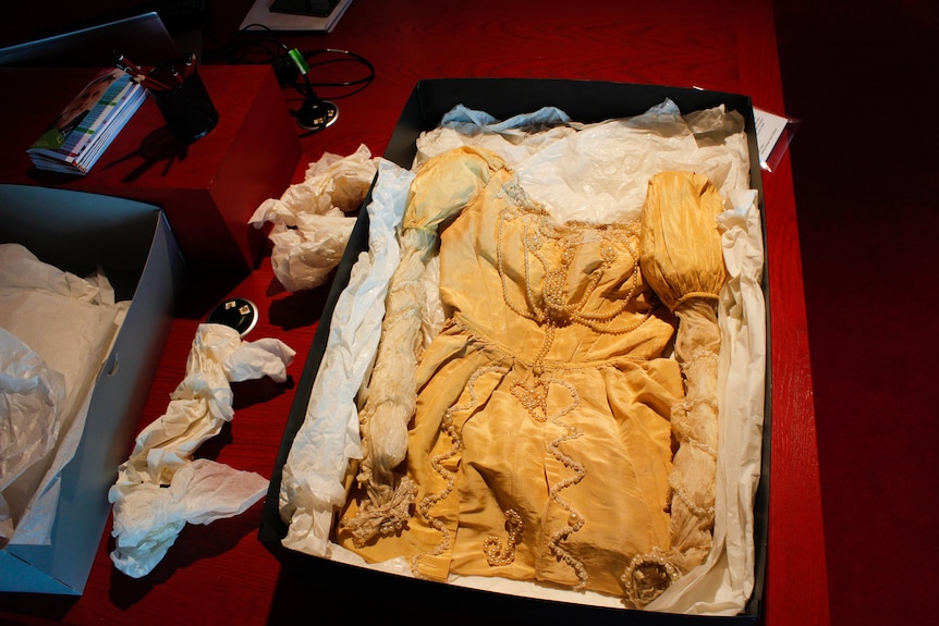 An old gold silk ball gown in a box with tissue paper