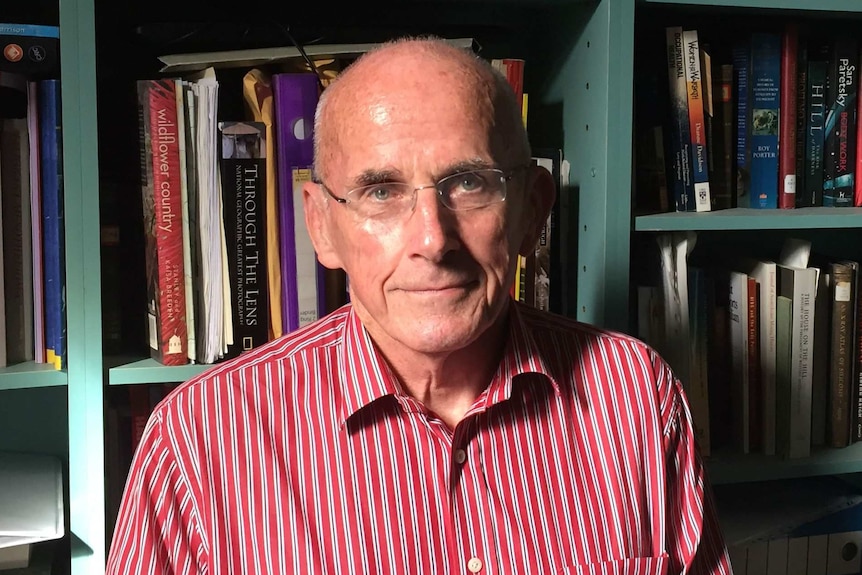 Man in striped shirt and glasses sits in front of bookcase