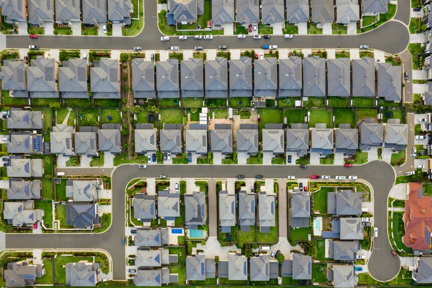 A birds-eye view of streets in a new-looking development. The rows of houses look similar and sit very close to each other.