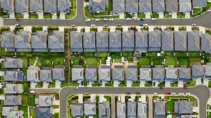 A birds-eye view of streets in a new-looking development. The rows of houses look similar and sit very close to each other.